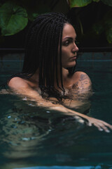 A woman with braids enjoying in a pool, surrounded by lush tropical leaves in a serene and intimate moment in Ubud, Bali, Indonesia