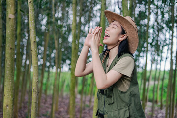 Woman in a green vest and cowboy hat enthusiastically calling out in a lush forest during daytime