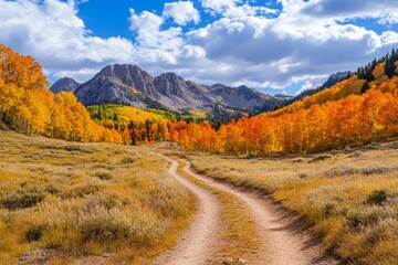 Obraz premium A winding hiking trail surrounded by brilliant autumn leaves invites adventure seekers to explore the serene beauty of nature. Mountains tower in the distance under a bright sky