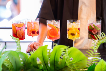 Colorful cocktails in tall glasses garnished with fruits and herbs, arranged on a bar counter. A...