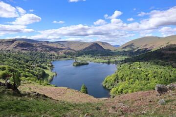 Wide view of Grasmere Lake with calm water, green trees and surrounding hills, taken from a hilltop. Lake District, England, UK.