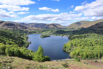 Fototapeta premium Panoramic view of Grasmere Lake with calm water, green trees and distant hills, seen from above on a hill. Lake District, England, UK.