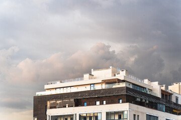 Modern residential building with a mix of brick and wood facade under dramatic evening clouds,...