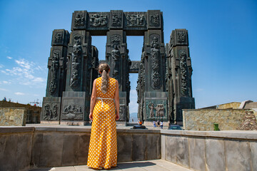 A girl in a yellow dress stands at the monument of the chronicles of Georgia