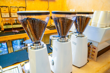 Three white professional coffee grinders stand on a counter, their hoppers filled with roasted...