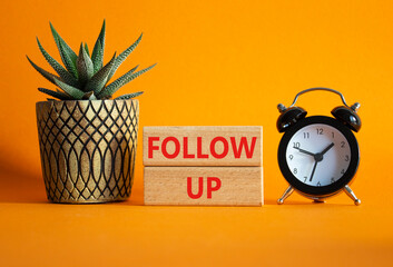 Follow up symbol. Concept word Follow up on wooden blocks. Beautiful orange background with alarm...