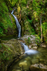 A serene waterfall cascades down mossy rocks in a vibrant forest near Klaus an der Pyrhnbahn,...