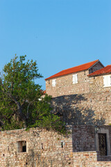 Obraz premium A fragment of the stone medieval fortress of Sveti Stefan island-hotel, on the Adriatic coast, Montenegro. Details. Vertical