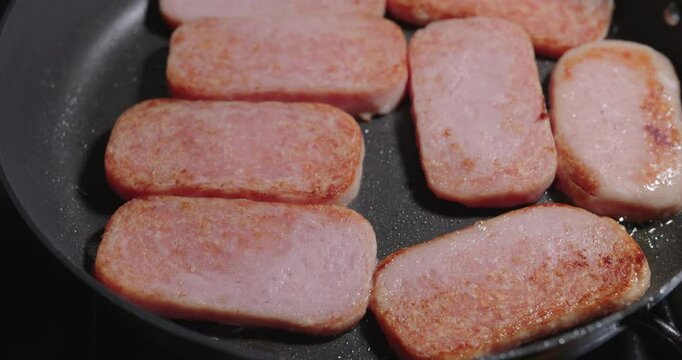 Closeup of slices of Spam, a popular canned cooked meat product, cooked in a frying pan