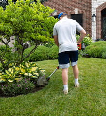 A self motivated teenage boy edges the garden  methodically carving clean lines between lawn and flowers. Sweat glistens as he works, shaping the soil with precision and pride in the hot, humid sun