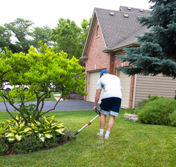 A self motivated teenage boy edges the garden methodically carving clean lines between lawn and flowers. Sweat glistens as he works, shaping the soil with precision and pride in the summer sun.