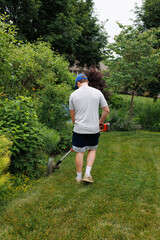 A self motivated teenage boy edges the garden methodically carving clean lines between lawn and flowers. Sweat glistens as he works, shaping the soil with precision and pride in the summer sun.