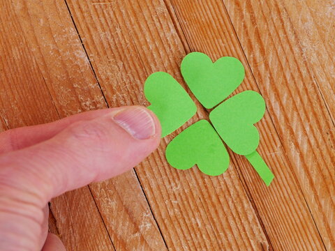A hand is touching a green paper heart that is part of a four leaf clover - Powered by Adobe