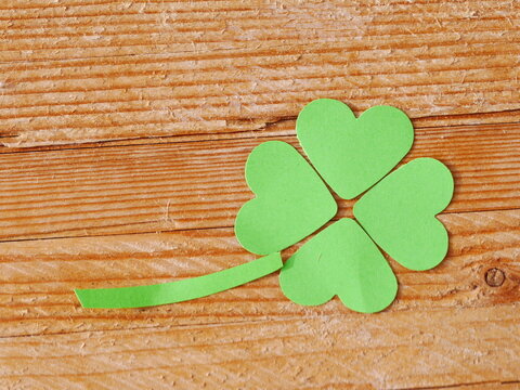 A green paper clover with four hearts on it is on a wooden surface