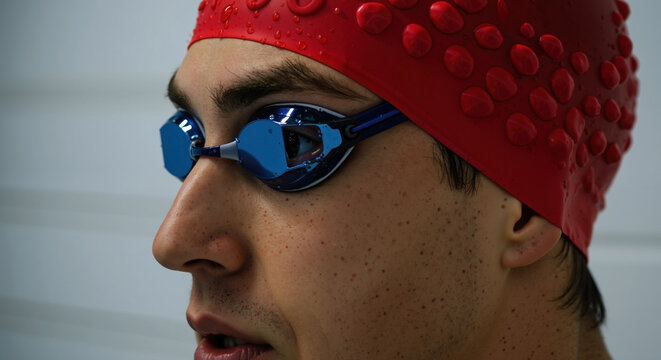 Male swimmer wearing red swimming cap and blue goggles preparing for competitive race in pool. Professional athlete portrait with sports equipment