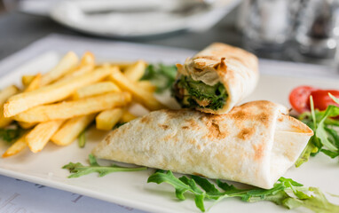 Fresh tortilla wrap served with golden fries and arugula on a white plate close-up. Casual dining, fast lunch and tasty street food in a modern restaurant setting.