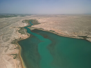 Aerial view of a winding river delta merging with turquoise water. Dry steppe surrounds Kuimazar...