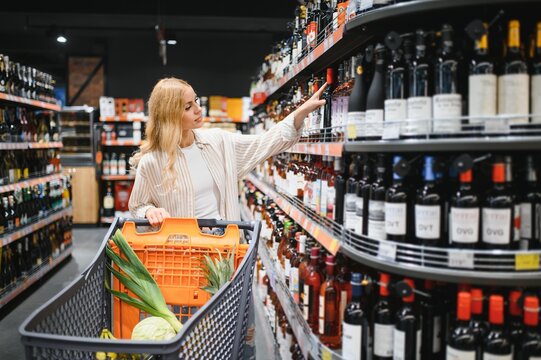 girl chooses wine in supermarket. girl reads labels on bottles of wine in supermarket