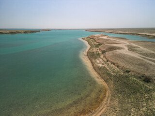 Aerial view of Kuimazar Reservoir shoreline curving around arid land in Uzbekistan. The blue-green...