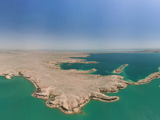 Aerial view of the Kuimazar Reservoir showing striking blue-green waters and dry desert landscape in Uzbekistan. The calm lake contrasts with the arid surroundings, creating visual harmony