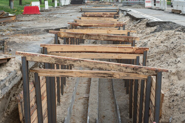 Trench construction with wooden and metal bracing for underground infrastructure installation on a city street.
