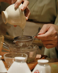 Green tea poured carefully through metal strainer.