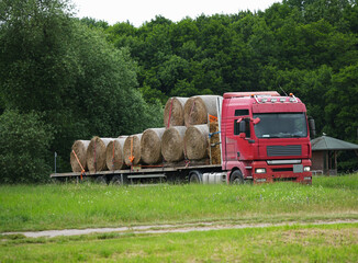 Red truck with trailer transporting hay or straw bales in the countryside