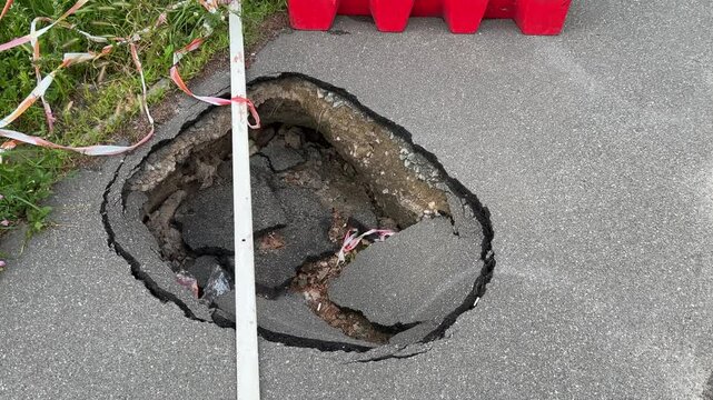 Asphalt sidewalk collapsed large hole plastic barrier fence road construction safety