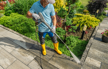 Man Pressure Washing a Stone Pathway in a Vibrant Garden During Sunny Weather