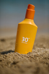 Sunscreen bottle with SPF  on a sandy beach, ideal for summer sun protection.