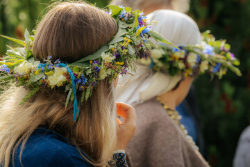Two women in traditional attire wear elaborate wildflower crowns during a cultural celebration...