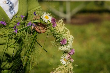Close-up of a person holding a handwoven floral crown made of daisies, grasses, and wildflowers,...