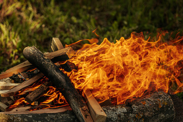 Bright orange flames rise from burning firewood arranged on a stone surface in an outdoor setting,...