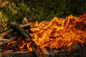 Bright orange flames rise from burning firewood arranged on a stone surface in an outdoor setting,...