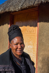 village single old african woman with dreadlocks braids in a headscarf sited in front of the house , in the yard, close portrait