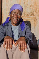 village single old african woman with headscarf sited in front of the house , in the yard, close portrait