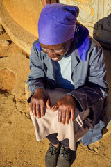 village single old african woman with headscarf sited in front of the house , in the yard, top portrait