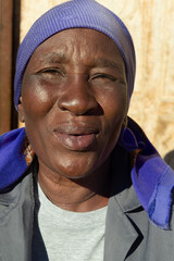 village single old african woman with headscarf sited in front of the house , in the yard, close portrait