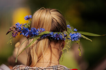 Close-up of a young woman’s blonde ponytail adorned with a vibrant blue cornflower crown, set...