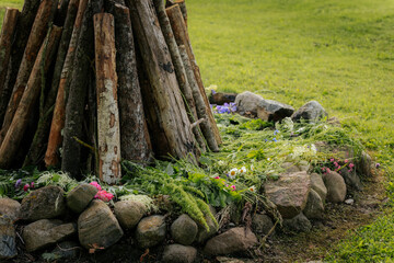 A wooden bonfire setup surrounded by rocks and fresh wildflowers on green grass, prepared for an...