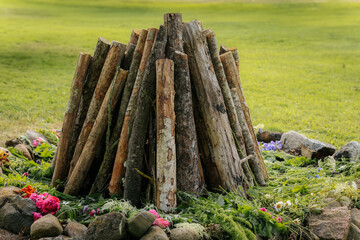 A wooden bonfire setup surrounded by rocks and fresh wildflowers on green grass, prepared for an...