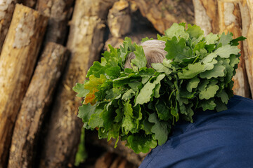 A mature man in a blue shirt wears a large oak leaf crown, participating in a traditional outdoor...