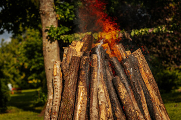 Tall bonfire burning intensely with orange flames reaching high, surrounded by rocks and trees...