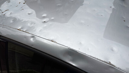Detail of a car roof severely damaged by hail, with numerous visible dents caused by the impact of...