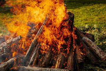 Intense orange flames engulf burning firewood in a large bonfire, with vivid textures of charred...