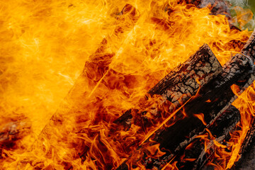 Intense orange flames engulf burning firewood in a large bonfire, with vivid textures of charred...