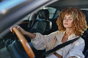 young woman driving car wearing seatbelt with curly hair and casual jacket, focused expression, daylight, modern vehicle interior, safe driving concept