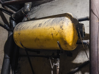 An old, dirty boiler hanging in the basement, surrounded by pipes and cobwebs, symbolizing the wear and neglect of the installation
