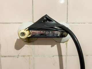Provisionally repaired shower holder, wrapped with black insulating tape, on an old, pink, dirty...