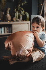 Cute child sitting on the floor trying to inflate a copper balloon, in a warm, home environment